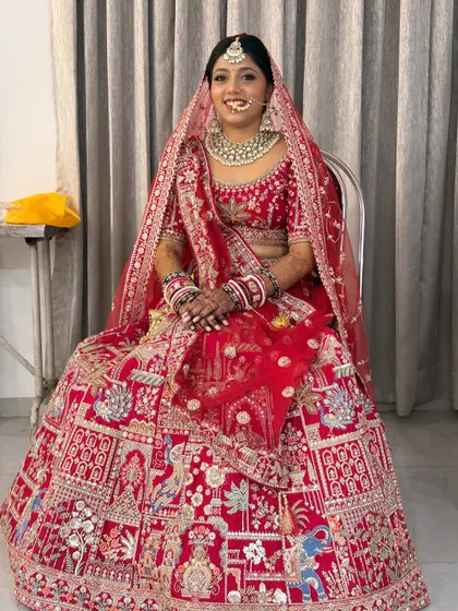 The bride seated, giving a full view of her intricately embroidered lehenga. The makeup and hair are styled to perfection.