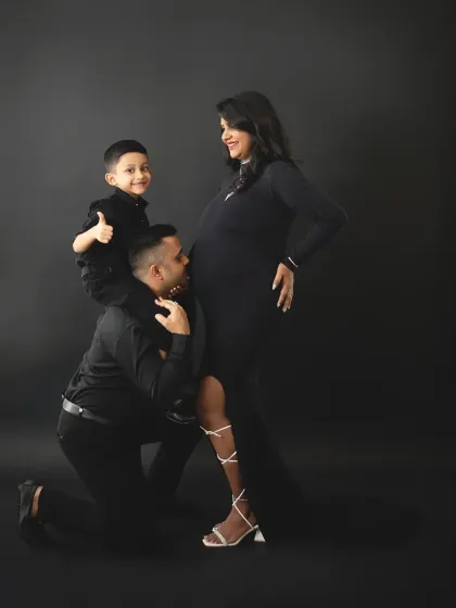 A fun and loving family maternity pose. The big brother gets a lift on dad's shoulders while dad kisses the baby bump, showing love for both his children.