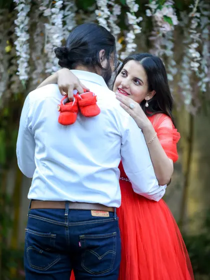 A creative and sweet reveal. The mom-to-be surprises her partner with a tiny pair of red baby shoes during their outdoor shoot.