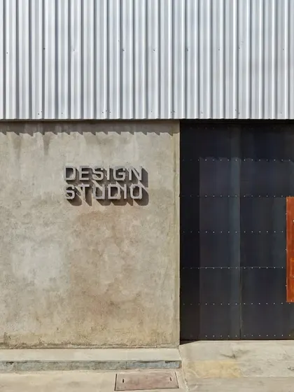 The entrance to the Automobile Design Studio makes a bold statement with raw concrete, corrugated metal, and a massive, riveted steel door. The custom-cut "Design Studio" signage adds a refined detail to the rugged, industrial material palette.