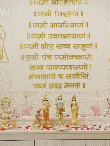 A full view of a beautifully arranged home mandir. It features my porcelain Ram Darbar, a Ganesha idol, and other divine figures against a wall inscribed with the sacred Navkar mantra, creating a complete spiritual sanctuary.
