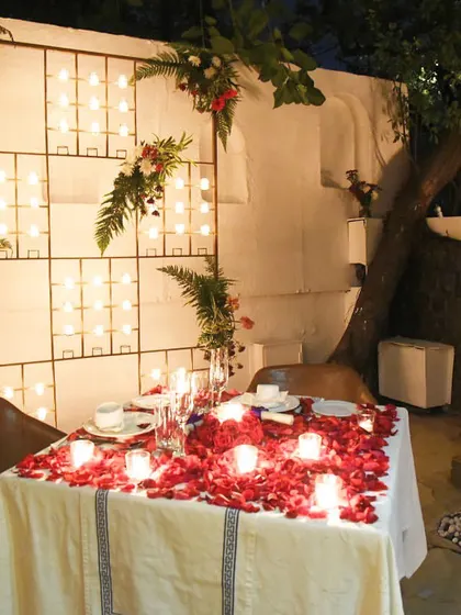 The combination of a candlelit wall, floral arrangements, and a table covered in rose petals makes for an incredibly romantic and photogenic setting.