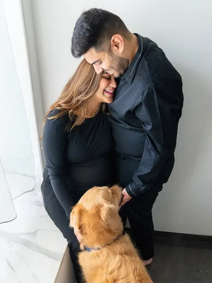 A candid moment from a maternity shoot where an expecting couple shares a laugh while their golden retriever looks on.