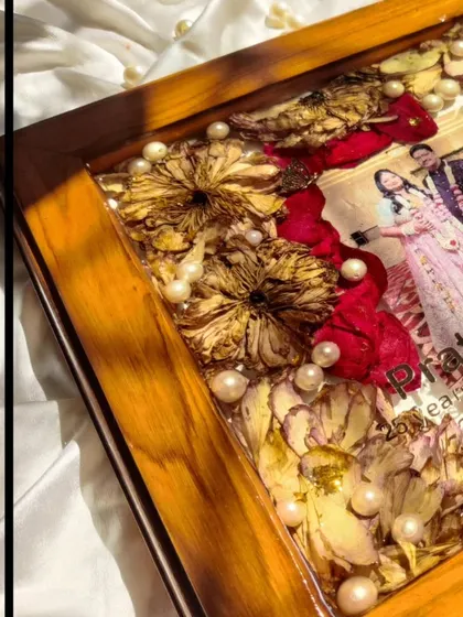 A close-up on the corner of the anniversary frame, showing the detail of the teakwood and the glossy finish of the resin over the preserved flowers.