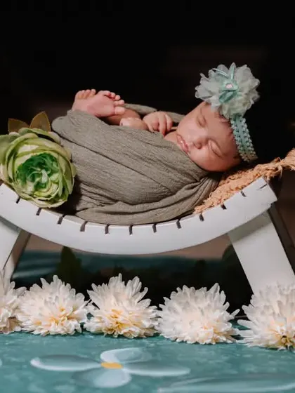 This newborn is beautifully wrapped and posed on a white bench, accented with delicate white and green flowers for a fresh, clean aesthetic.