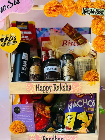 A full view of the two-tiered Rakhi hamper, decorated with marigold pom-poms and filled with coffee, snacks, and more.