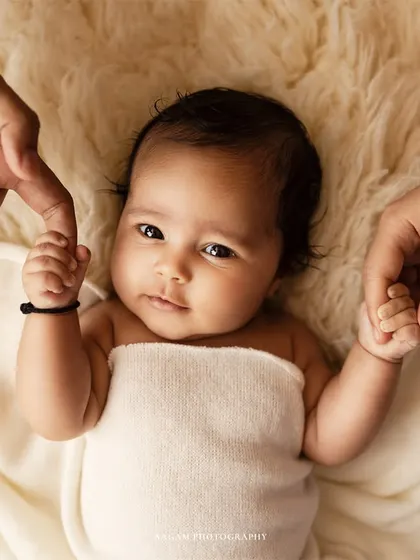 A sweet newborn portrait, with the baby looking directly at the camera while holding their parents' hands. A precious memory of their first few weeks.