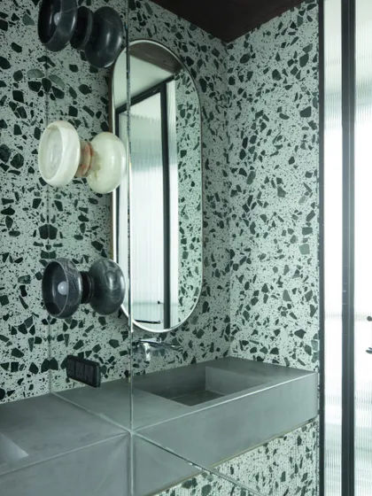 A close-up of the custom hand-chiseled stone wall lights, which resemble yo-yos, adding a whimsical and bespoke touch to the terrazzo-clad bathroom.