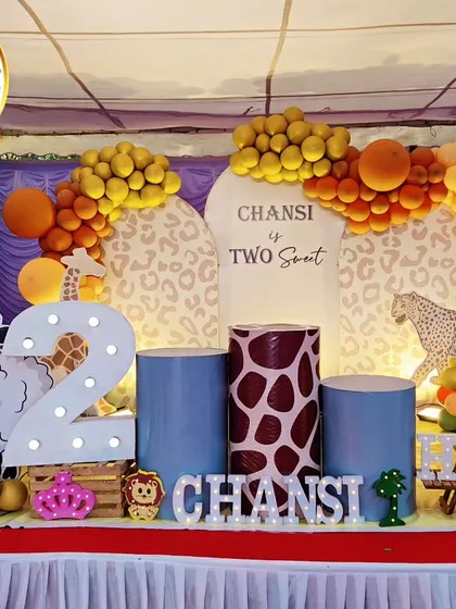 A complete jungle-themed stage for a second birthday. The setup includes a 'Two Sweet' backdrop, animal-print plinths, a large light-up number '2', and cutouts of a sheep and giraffe.