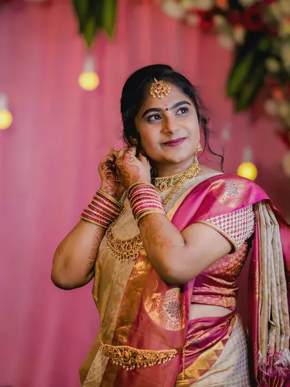 A happy bride getting ready for her big day. This look features a soft pink and gold theme, with makeup that enhances her features and complements her cream and pink silk saree.