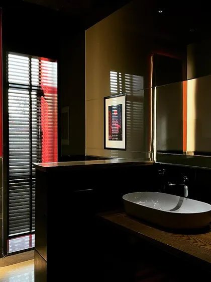 A bathroom in a workspace designed with a focus on darkness and contrast. The interplay of shadow, reflection, and sharp accents of red light creates a bold and memorable experience.