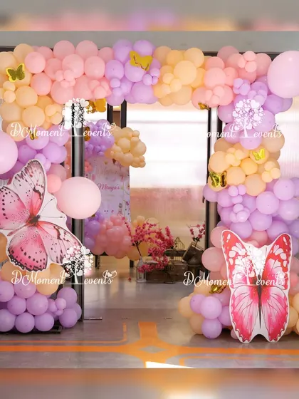 A beautiful pastel balloon arch decorated with large butterfly cutouts, creating a perfect entrance or photo spot for a garden party.