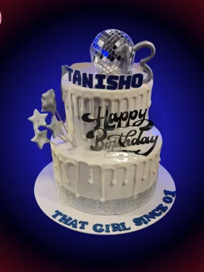 A still shot of the two-tiered disco birthday cake. The dripping white icing and rhinestone ribbon add to the glamorous party feel.