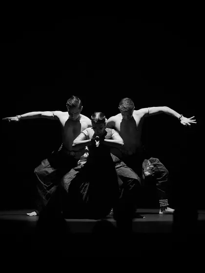 A black and white photograph capturing the essence of 'ĀBHA'. The focus is purely on the form and the emotional connection between the three performers.