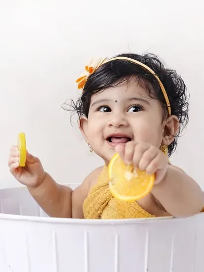 A happy baby playing with orange slices in a tub. The bright colors and cheerful expression make this a wonderfully vibrant and fun photo.