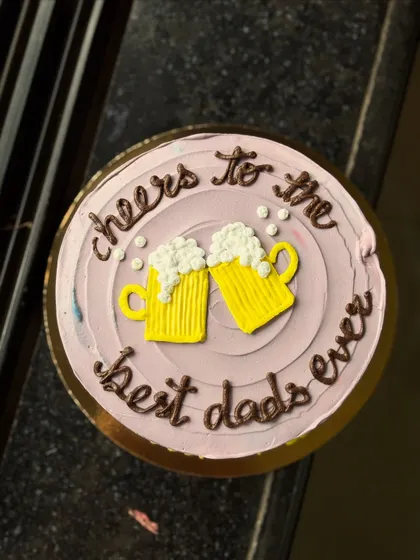 A fun cake for Father's Day, saying "cheers to the best dads ever" with two frothy beer mugs. It's a great way to celebrate dad with a bit of fun.