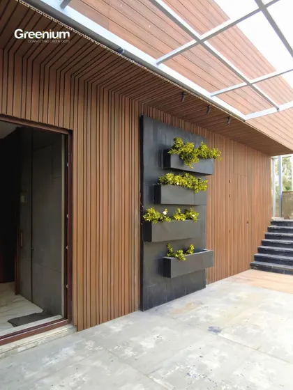 The "after" shot of the Pitampura terrace wall. The finished wall features beautiful wooden paneling and a modern black planter rack, creating a warm and inviting backdrop.