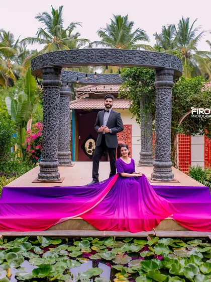 A grand portrait on a stage surrounded by water. The bride's vibrant purple and pink gown creates a stunning visual against the natural and architectural elements.
