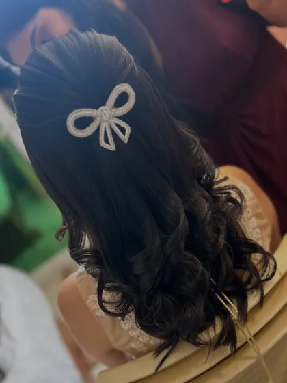 A still shot showing the detail of the pearl bow accessory on this chic half-up, half-down hairstyle. It's a modern and playful touch for any celebration.
