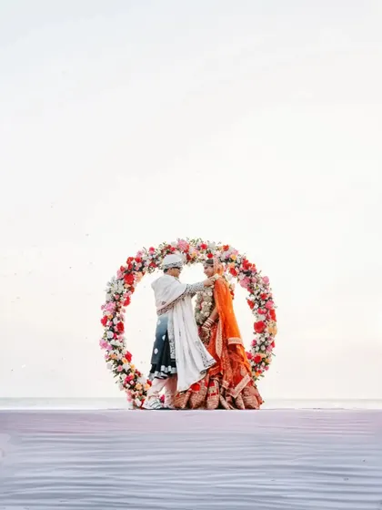 A stunning shot of the couple framed by a circular floral mandap against the backdrop of the ocean.