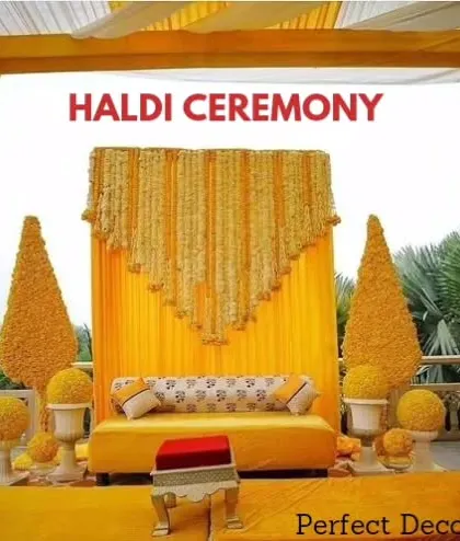 A classic Haldi ceremony backdrop. The design features a curtain of marigold flowers, cone-shaped floral arrangements, and a comfortable yellow diwan for the main seating.