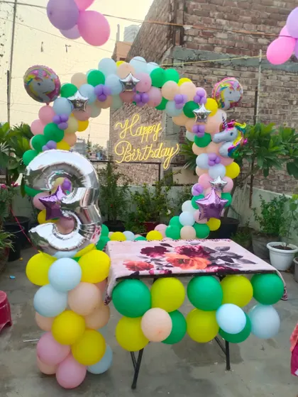 A unicorn-themed 3rd birthday setup on a rooftop. The pastel-colored balloon arch around the cake table looks beautiful in an outdoor setting.