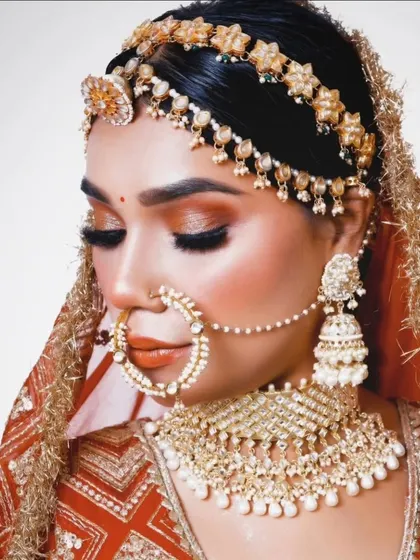 A classic bridal pose showcasing a pearl and gold-toned jewellery set. The matha patti, choker, and nath create a complete and elegant look.