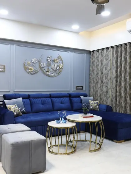This full view of the living area shows the L-shaped sofa, nested tables, and elegant wall decor. The layout is designed for comfortable lounging and social gatherings, with sheer curtains diffusing natural light.