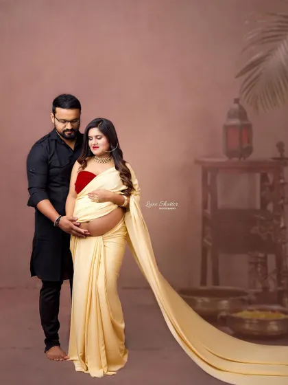 A graceful maternity portrait showcasing a beautiful cream-colored saree with a long, flowing trail. This image combines traditional elegance with a touch of modern drama.