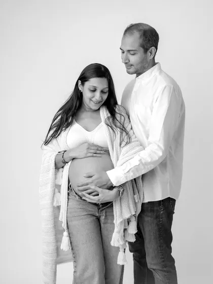 A casual and intimate black and white portrait. The mom-to-be in jeans and a simple shawl creates a relaxed and authentic image of a couple eagerly awaiting their baby.