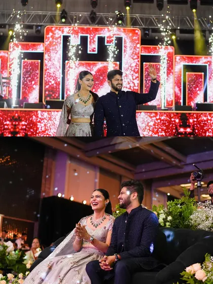 The grand entry of the happy couple at their Sangeet. They are greeted with sparklers and applause as they walk onto a stage with a large, illuminated 'H' monogram.