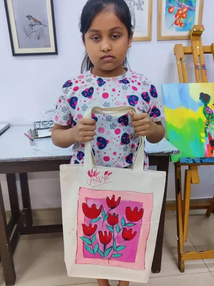 A young girl proudly holds up the tote bag she painted herself in one of our creative workshops.