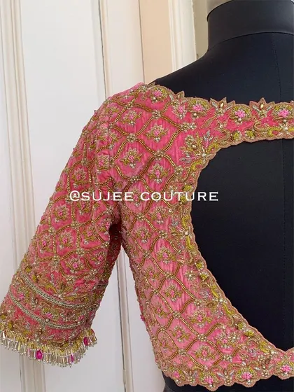 A heavily embellished back design on a pink bridal blouse. This piece features a large keyhole cutout, with the entire surface covered in a rich jaal pattern of zardozi and pearl work.
