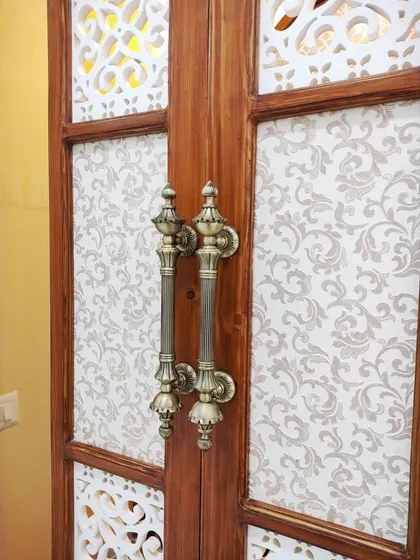 A close-up of the ornate brass handles on the pooja room doors. These details are carefully selected to complement the traditional design and add a touch of luxury.
