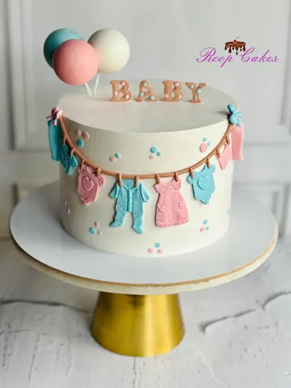An adorable baby shower cake with a clothesline of tiny fondant outfits, perfect for welcoming a new baby.