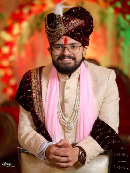 A formal seated portrait of the groom. His calm and composed demeanor is captured beautifully against the vibrant floral decor of the wedding stage.