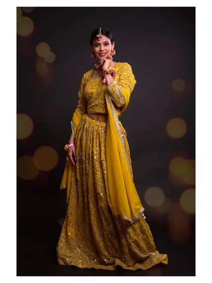 A full-length shot of a model in a beautiful yellow lehenga. The bokeh background adds a festive and magical touch.
