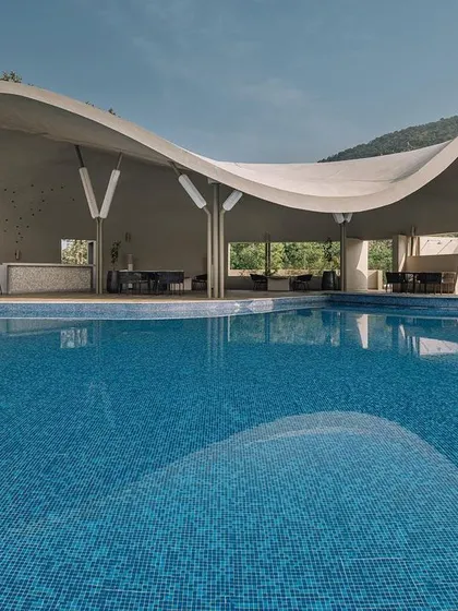 The same Aqua Pool & Spa project seen in daylight, where its sweeping, fluid form and parametric ferrocement roof are fully visible. The design captures panoramic views of the Nandi Hills, creating a seamless connection between the built environment and the vast outdoors.