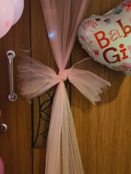 A detailed look at the door decoration, featuring a pink tulle bow and a heart-shaped "Baby Girl" balloon. These small touches make the welcome feel extra special.