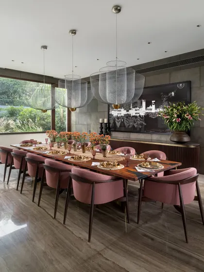 The dining room in the K Residence, set for a beautiful meal. The room overlooks an enclosed garden and is dominated by a solid wood table with a dancing brass base, surrounded by chairs upholstered in a soft dusty pink.