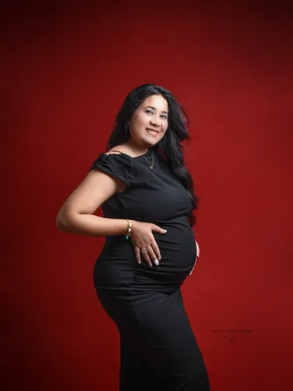 A classic and chic portrait. A simple, well-fitting black dress against a bold red background is a timeless choice for a maternity shoot.
