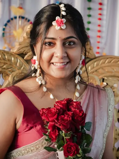 A bride's happiness is radiant. This close-up portrait during her Haldi ceremony captures her beautiful smile and the excitement of the moment, framed by a bouquet of fresh red roses.