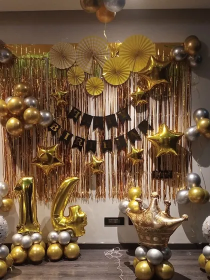 A royal-themed 14th birthday decoration in gold and silver, featuring a foil curtain, number balloons, and a crown prop.