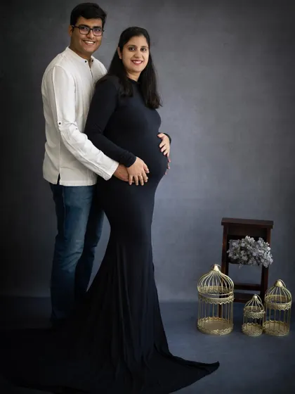 A classic couple's portrait against a simple grey backdrop. The focus is on their happy smiles and the shared excitement for their baby girl's arrival.