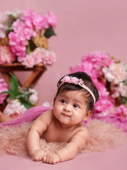 Tummy time is a big milestone! This photo captures a baby girl lifting her head and looking around, surrounded by soft pink textures and flowers.
