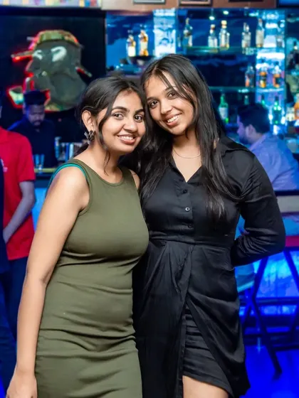 Two friends enjoying a night out, with the well-stocked bar visible in the background.