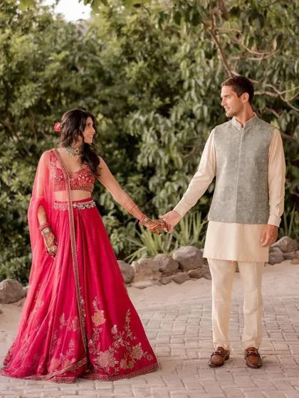 Tailored in togetherness. This shot captures the couple's coordinated Sangeet look, with her in a vibrant pink lehenga and him in a complementary pastel ensemble.