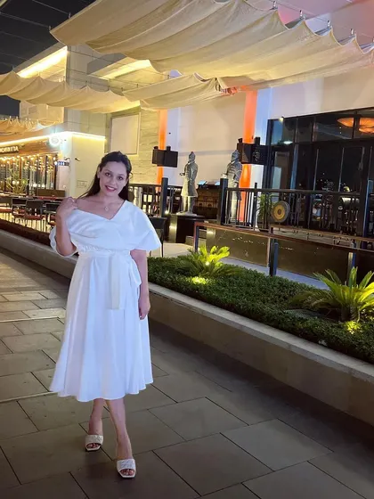 A client looking elegant in a custom all-white midi dress. The off-shoulder neckline and belted waist create a timeless and flowy silhouette, perfect for a special evening out.
