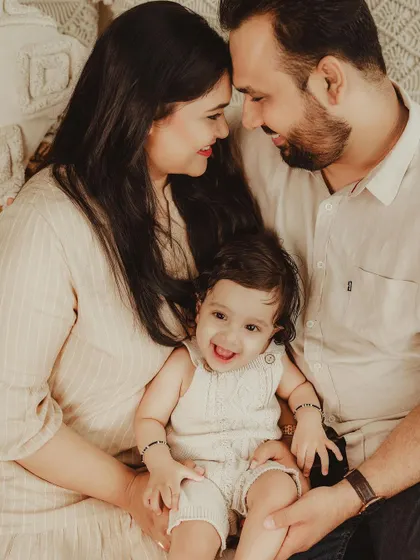 A close-up, joyful family portrait. The focus is on the genuine smiles and loving interaction between the parents and their happy baby.