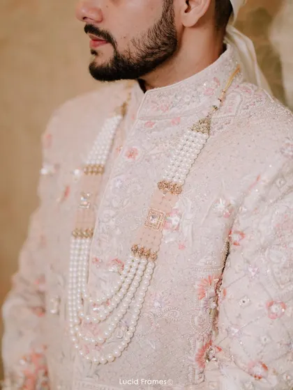 A detail shot of the groom's sherwani and the elegant pearl necklace (satlada), highlighting the richness of his wedding attire.
